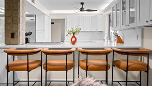 A modern kitchen with white cabinets, a central island with bar stools, and a ceiling fan. - Mini Resort w/ Mountain Backdrop | Heated Pool, Hot Tub, Sauna, Cold Plunge (Phoenix)