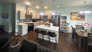 A modern kitchen with a central island, bar stools, and a dining area with a table and chairs. - Sophisticated 4 Bedroom Retreat (Montrose)
