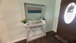 A hallway with a wooden console table, a framed painting, and a door with a frosted glass window. - Sophisticated 4 Bedroom Retreat (Montrose)