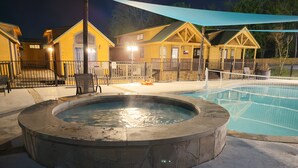 A hot tub surrounded by a pool, wooden cabins, and a fenced patio area. - Rustic Lake Cabin #215 with Pool and Lake Access (Willis)