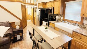 A modern kitchen with wooden cabinets, a central island, and a dining area with a brown leather couch and a small table. - Rustic Lake Cabin #215 with Pool and Lake Access (Willis)