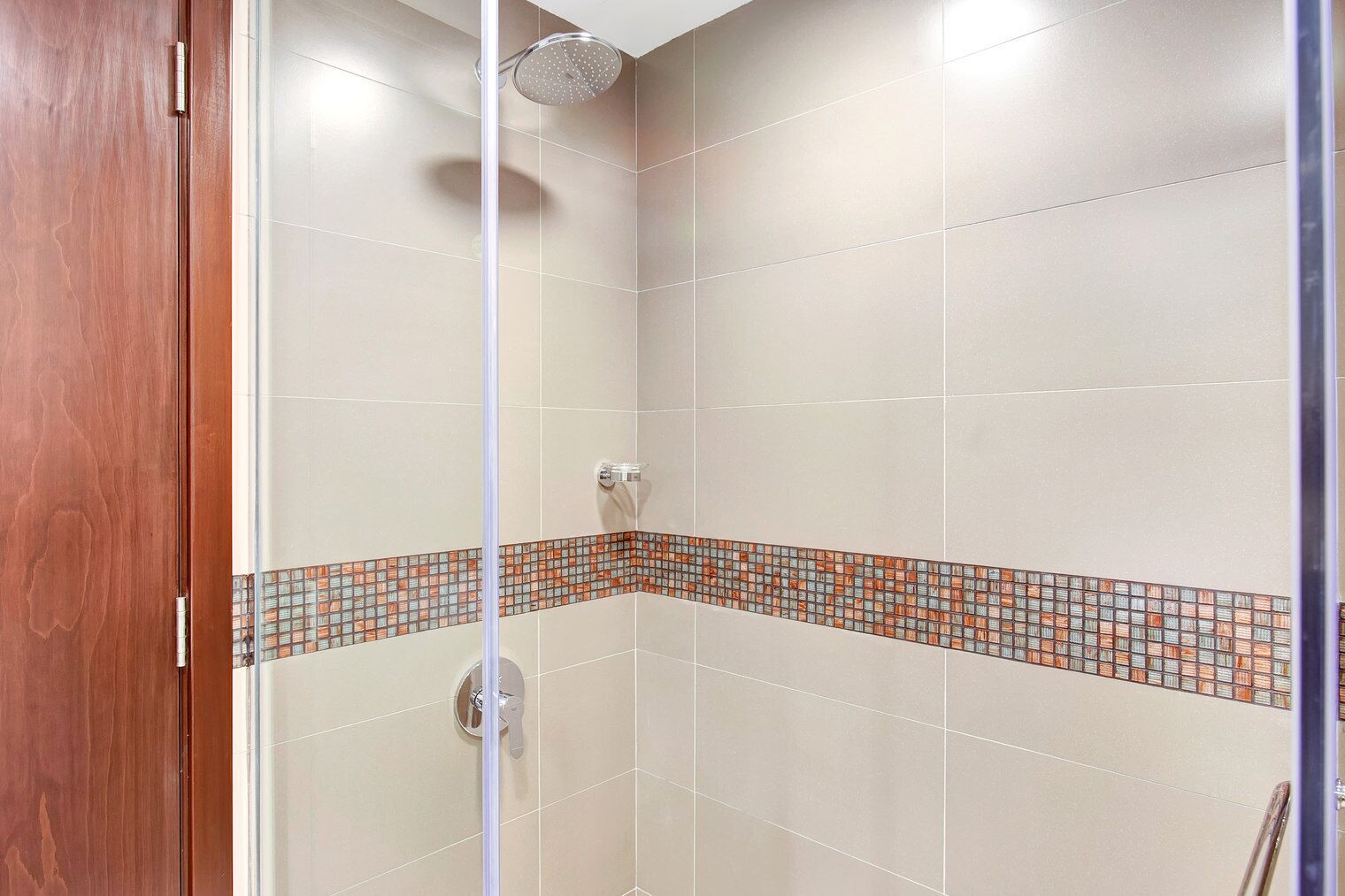 Een douche met een betegelde muur en een houten deur.