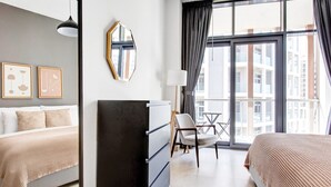 Ein modernes Hotelzimmer mit großem Fenster, einem Bett, einem Schreibtisch und einem Sessel.