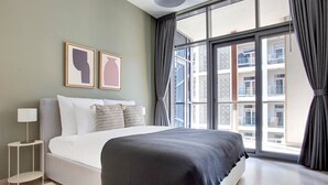 Ein modernes Hotelzimmer mit einem großen Bett, einem Nachttisch mit Lampe und Blick auf die Stadt durch raumhohe Fenster.