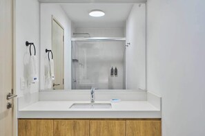 A modern bathroom with a white sink, a mirror, and a shower enclosure.
