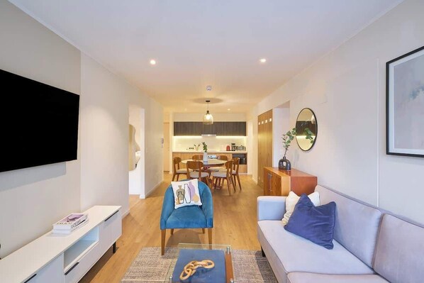 A modern living room with a flat-screen TV, a sofa, a coffee table, and a dining area with chairs and a table.