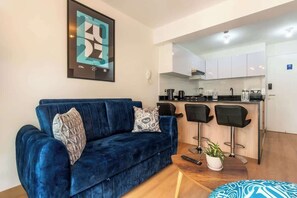 Ein Wohnzimmer mit einem blauen Sofa, einem Couchtisch und einer Küchenzeile mit einer Bar und zwei Stühlen.
