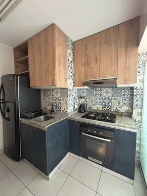 Eine kleine Küche mit Holdekor-Schränken, einem Edelstahl-Kühlschrank, einem Gasherd und einem eingebauten Backofen.