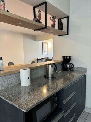 Eine moderne Küche mit Granitarbeitsplatten, einer Kaffeemaschine, einem Wasserkocher und einer Küchenpapierrolle.