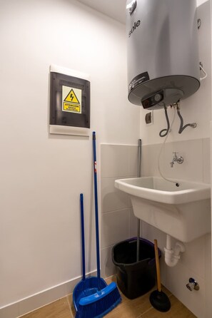 Ein Badezimmer mit Waschbecken, Toilette, einem Mopp, einem Besen und einem Mülleimer.