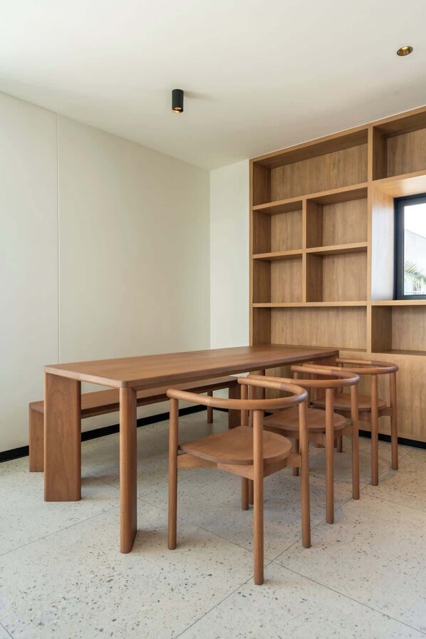 Ein schlicht eingerichteter Raum mit Holztisch und -stühlen, einer integrierten Bücherwand und einer Deckenleuchte.