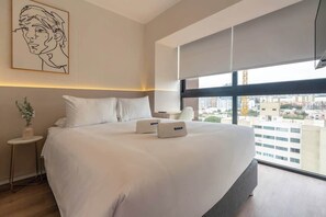 Ein modernes Hotelzimmer mit einem großen Bett, Blick auf die Stadt, einem kleinen Beistelltisch und einem Wandbild.