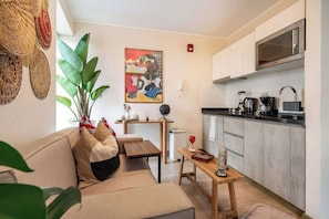 A compact living space with a sofa, a small dining table, a kitchen area with a microwave, and a wall-mounted artwork. - Geko | Functional Loft next to Malecón w/Pool (Barranco)