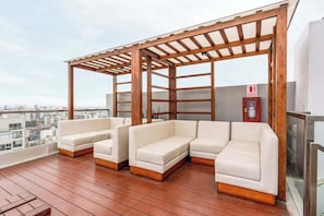 A rooftop terrace with a wooden pergola, white sofas, and a fire extinguisher. - Geko | Functional Loft next to Malecón w/Pool (Barranco)