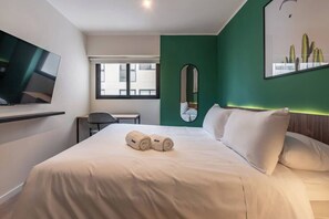 Ein Hotelzimmer mit Bett, Fernseher, Fenster und Spiegel, sowie einer Wand in Grünton.