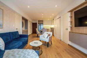A modern living room with a blue sofa, a white armchair, a round coffee table, and a TV mounted on the wall. - Geko | Spectacular 2BR near Malecon w/ balcony (Miraflores)