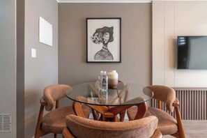 Ein moderner Essbereich mit einem Glastisch, Holzstühlen, einem gerahmten Kunstwerk und einem Fernseher an der Wand.