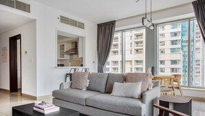 A modern living room with a grey sofa, a wooden coffee table, and a view of a residential building through large windows. - Blueground | Burj Residence Phase I & II, pool, nr Burj Khalifa (Dubai)