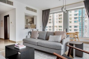Ein modernes Wohnzimmer mit einer grauen Couch, einem Holztisch und Blick auf ein Wohnhaus durch große Fenster.