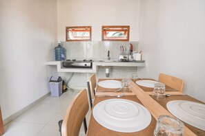 Una cocina con estufa, lavamanos y dos ventanas. Hay una mesa de comedor con platos y vasos.