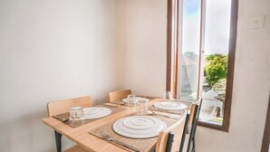 A dining table set with white plates, cutlery, and glasses, with a view of a garden through a window. - Moringa Pandawa Guest House (Kutuh)