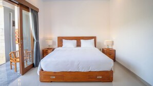 A large bed with wooden headboard and footboard, two bedside tables with lamps, and a sliding glass door leading to an outdoor area. - Moringa Pandawa Guest House (Kutuh)