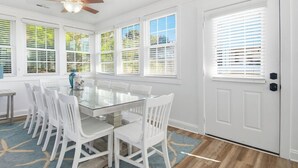 A dining area with a glass table surrounded by white chairs, large windows with blinds, and a ceiling fan. - Walk to the Ocean • Beach Access • Furnished Deck (North Myrtle Beach)