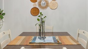 Uma sala de jantar com mesa de madeira, cadeiras brancas, um candelabro e detalhes decorativos de parede em tecido.