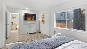 Quarto com cama, televisão presa na parede, janela e porta que dá para outro cômodo.