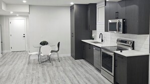 A modern kitchen with dark cabinets, a stainless steel refrigerator, and a built-in oven. - Cozy on 516! Cozy & Comfy 1 bedrm basement suite, Close to Calgary Int'l Airport (Airdrie)
