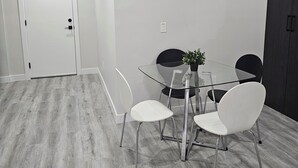 A modern dining area with a glass table, white chairs, and a dark wooden cabinet. - Cozy on 516! Cozy & Comfy 1 bedrm basement suite, Close to Calgary Int'l Airport (Airdrie)