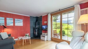 A living room with a fireplace, a sofa, a TV, and a view of a garden through large windows. - Spacious Apartment • Ski-in, Ski-out • Terrace (Lauterbrunnen)