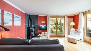A modern living room with a sofa, a TV, a fireplace, and a view of the outdoors. - Spacious Apartment • Ski-in, Ski-out • Terrace (Lauterbrunnen)