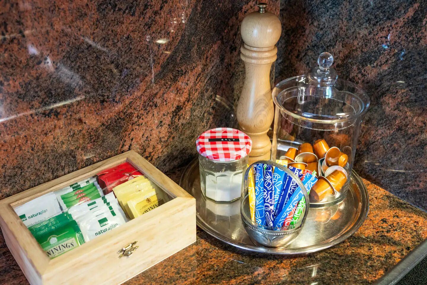Un comptoir de cuisine sur lequel se trouve une boîte en bois contenant divers aliments, un salier, un poivrier et un bocal en verre avec un couvercle à carreaux.