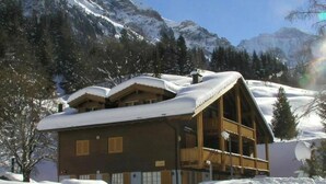 A chalet-style building with a sloped roof, surrounded by snow-covered mountains and trees. - Spacious Apartment • Ski-in, Ski-out • Terrace (Lauterbrunnen)