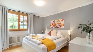 A modern hotel room with a large bed, a bedside table, a window with curtains, a radiator, and a painting on the wall. - Spacious Apartment • Ski-in, Ski-out • Terrace (Lauterbrunnen)