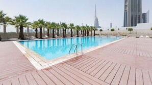 A rooftop pool with palm trees and lounge chairs, surrounded by a wooden deck. - Blueground | DIFC, pool, nr Dubai Mall (Dubai)