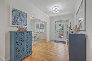Een gang met een blauwe kast, een eethoek met stoelen en een deur naar buiten.