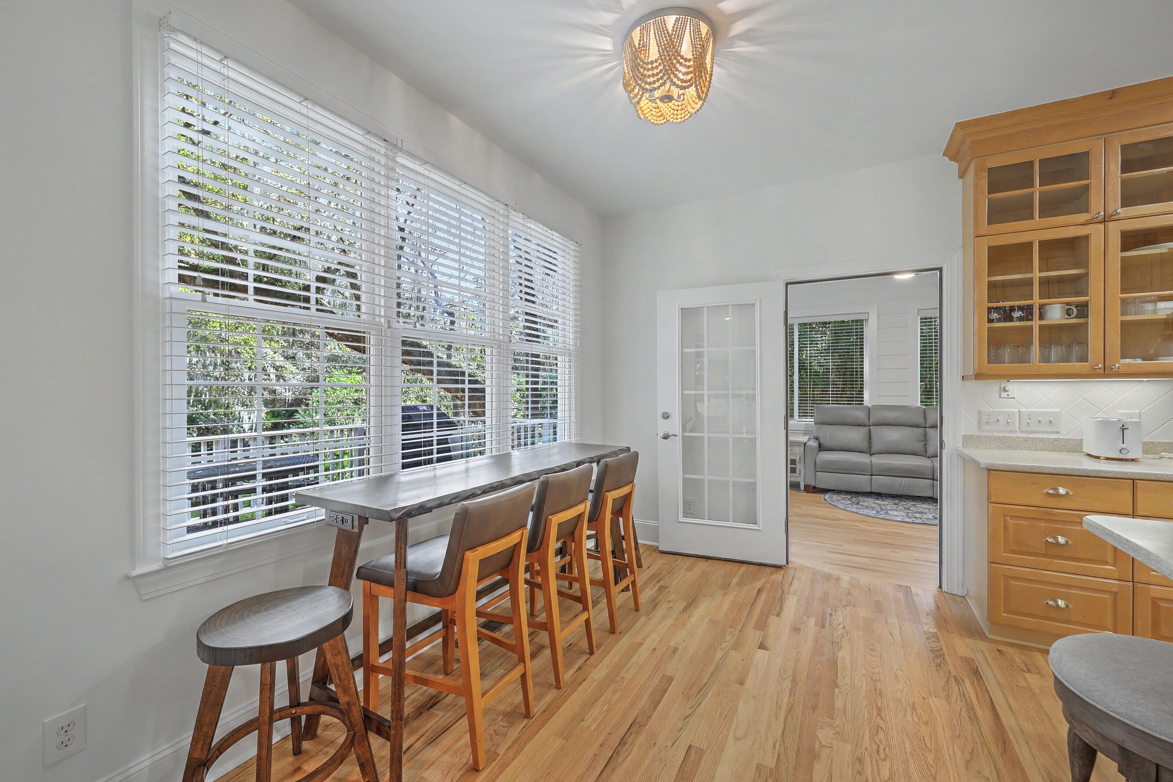Una cocina con barra de madera, armarios blancos y vistas al exterior a través de amplios ventanales con persianas.