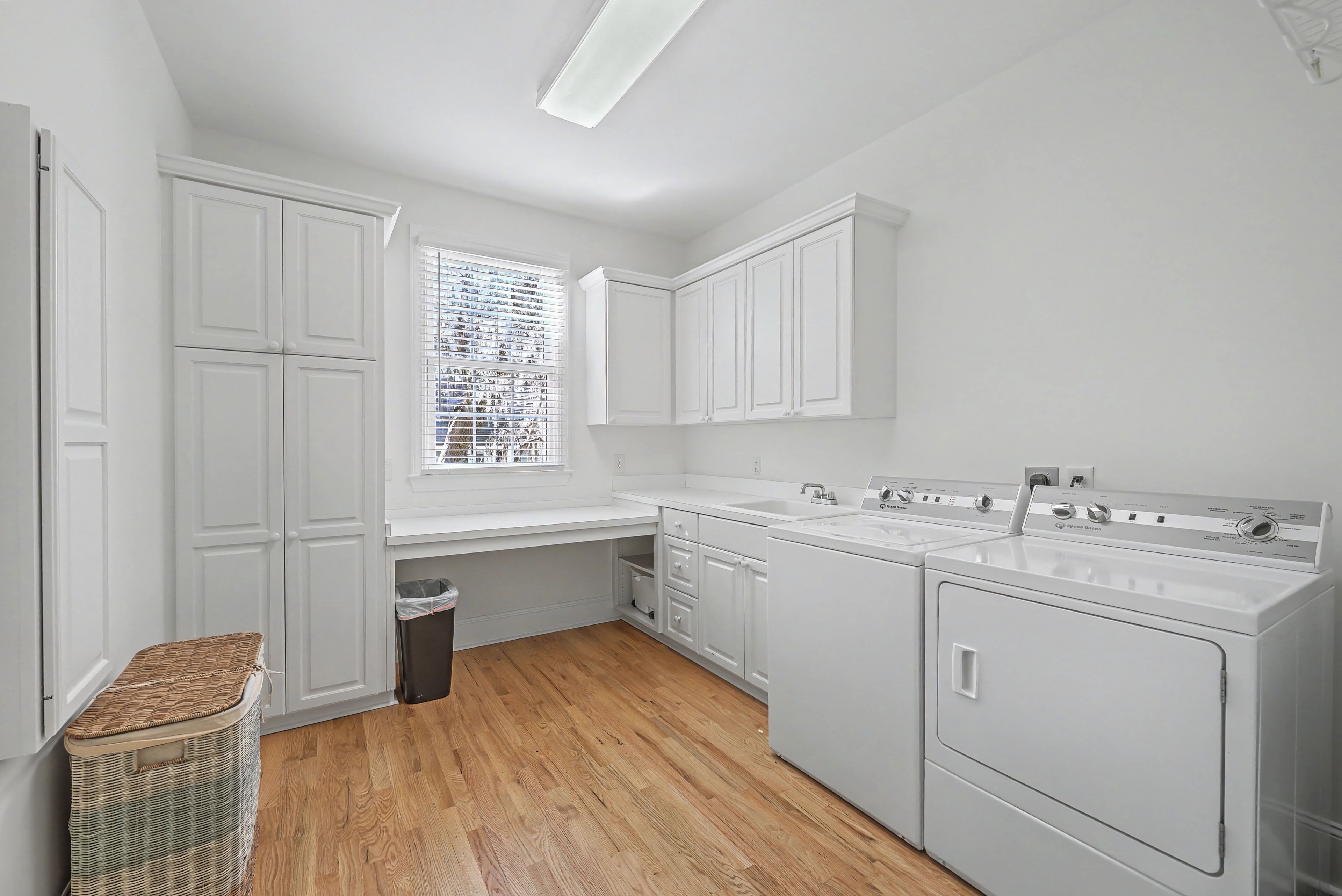 A laundry room with white cabinets, a washing machine, and a window with blinds.