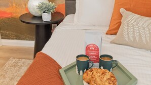 Ein ordentlich bezogenes Bett mit einem Tablett mit Speisen und Getränken, einer Lampe und einer kleinen Pflanze auf einem Nachttisch.