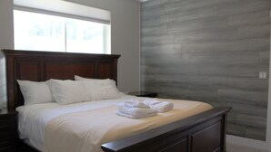 Een slaapkamer met een groot bed, een houten hoofdbord, een nachtkastje en een raam met blinds.