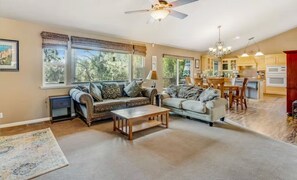 Open-plan living room with sofas and large windows overlooking trees, connected to the kitchen. - Cozy Mountain Retreat with Hot Tub & Game Room (Groveland)