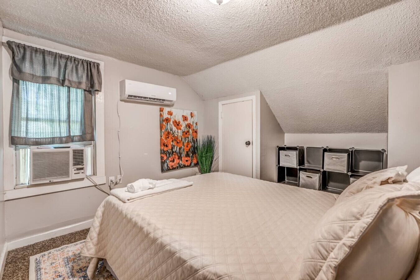 Ein Schlafzimmer mit einem großen Bett, einer Klimaanlage, einem Gemälde und Stauraumeinheiten.