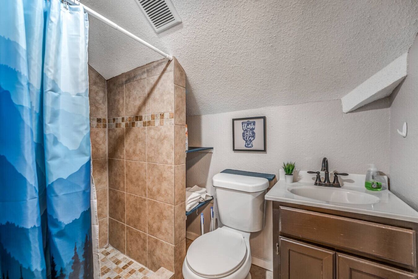 A bathroom with a shower, toilet, sink, and a framed sign on the wall.