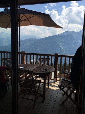 Eine Holzterrasse mit Tisch und Stühlen, mit Blick auf eine gebirgige Landschaft.