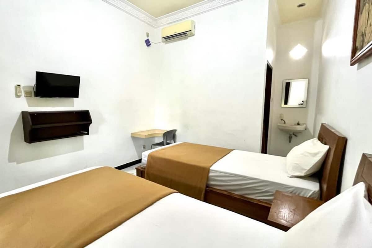 A hotel room with two beds, a TV, a bedside table, a mirror, and a small sink.