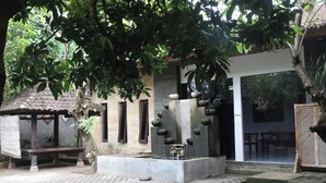 A courtyard with a stone fountain, a wooden bench, and a building with a tiled roof. - Adhya Guest House (Mataram)