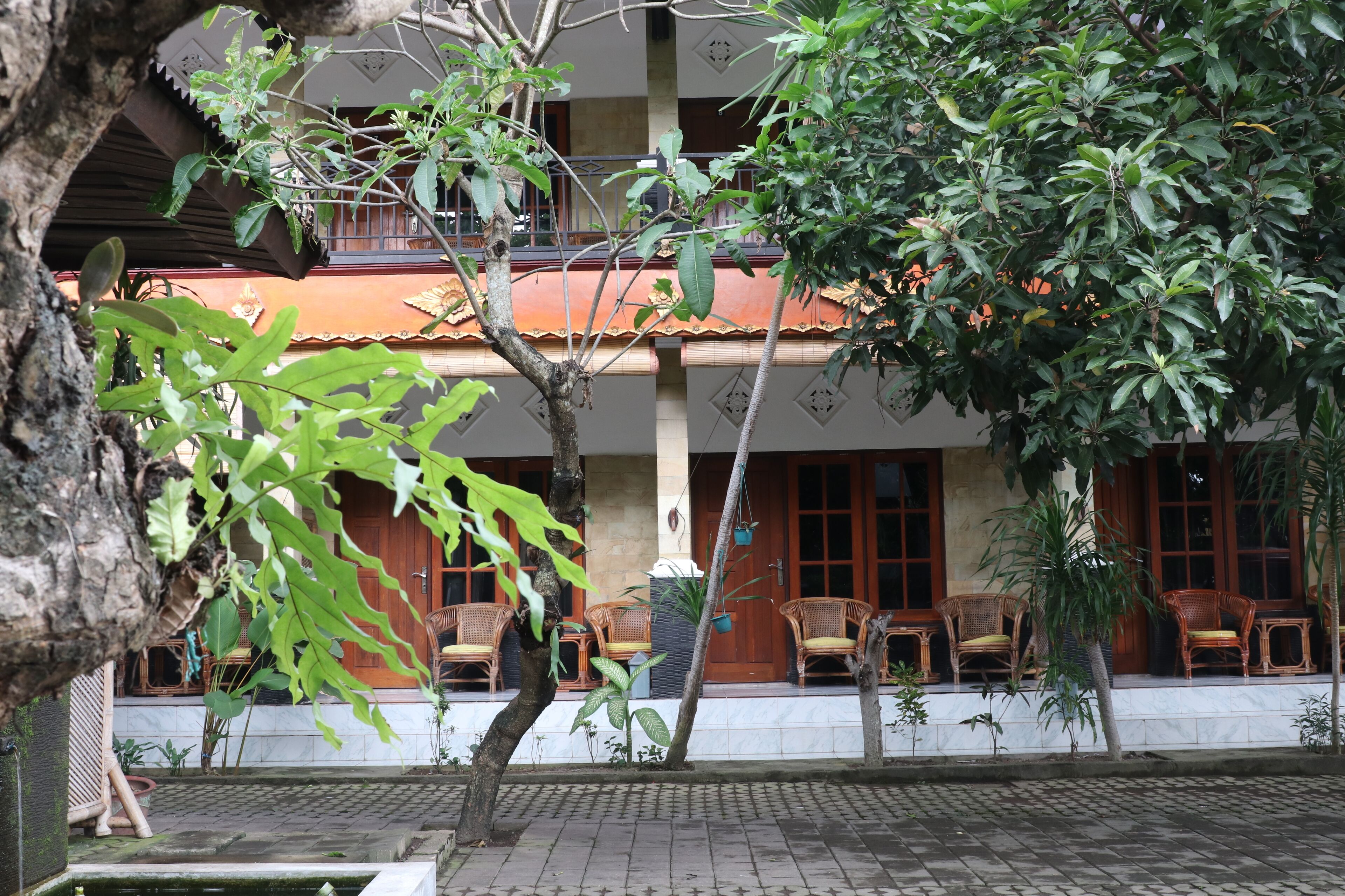 Ein Gebäude mit einer gefliesten Terrasse, Korbmöbeln und einem Baum im Vordergrund.