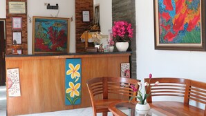 A reception desk with framed artwork, a wooden reception area, and a seating area with a vase of flowers. - Adhya Guest House (Mataram)